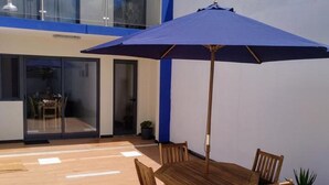A patio with a wooden table and chairs, a blue umbrella, and a small potted plant. - California House in Ribeira Grande (Ribeira Grande)