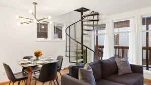 Un intérieur moderne avec un escalier en colimaçon, un coin repas avec une table dressée pour deux personnes et un espace salon confortable avec un canapé.