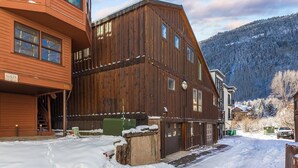 Un bâtiment en bois avec un escalier menant à un deuxième étage, entouré d’un sol recouvert de neige et avec une montagne boisée en arrière-plan.
