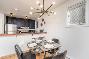 A modern kitchen with dark cabinets, a stainless steel refrigerator, and a glass dining table set for four. - Little Gem, Prime Location | 1BR + Loft | Walk to Ski & Main Street (Telluride)