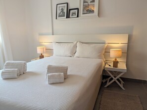 A neatly made bed with white linens, two bedside lamps, and a small bedside table.