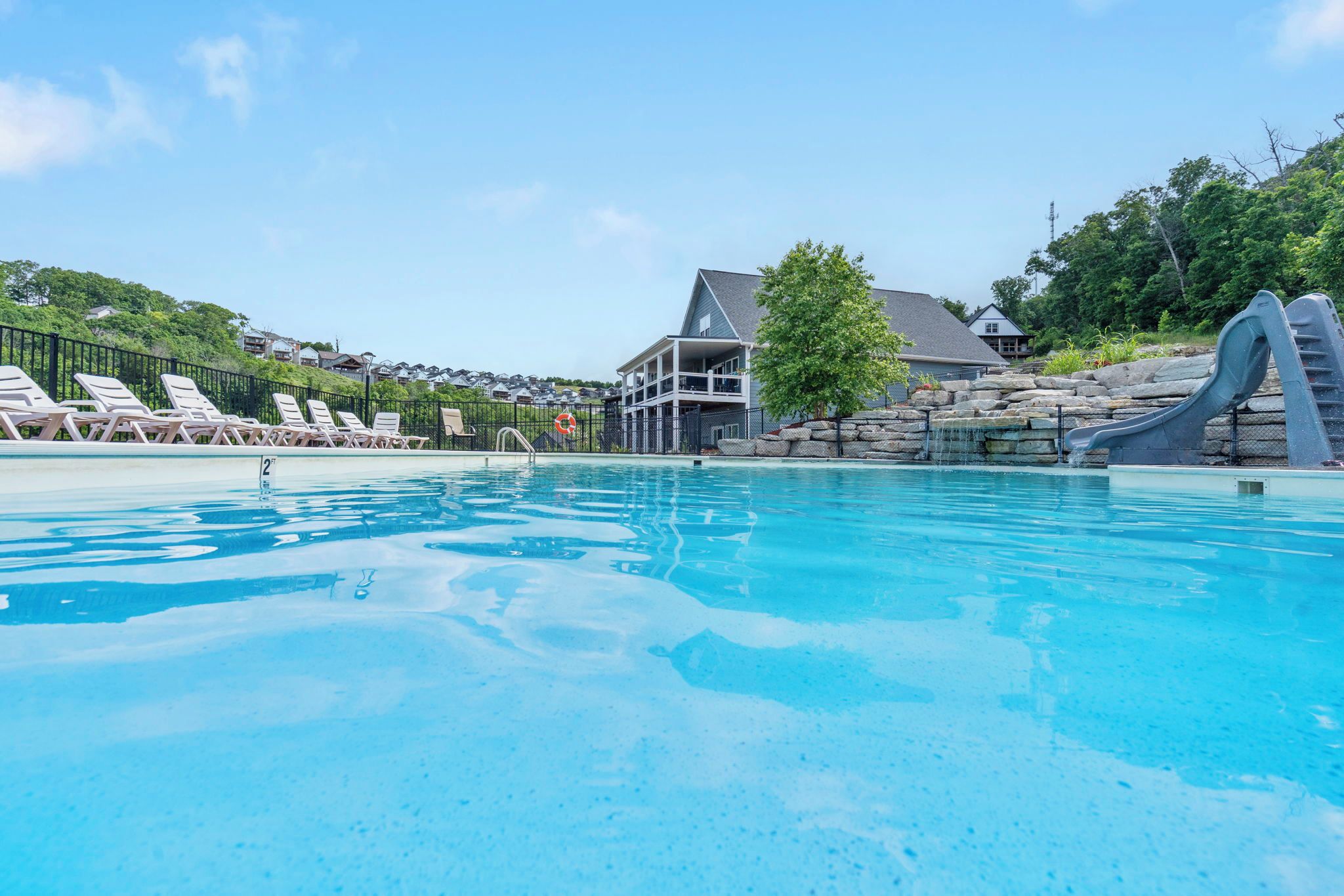 A swimming pool with lounge chairs, a lifebuoy, a building with a balcony, and a water slide.