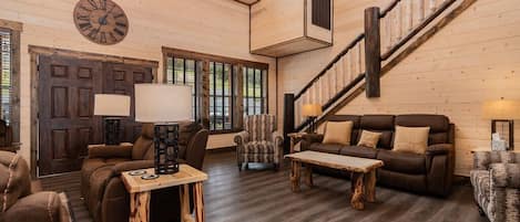 A spacious living room with a wooden floor, a large clock, and a staircase.