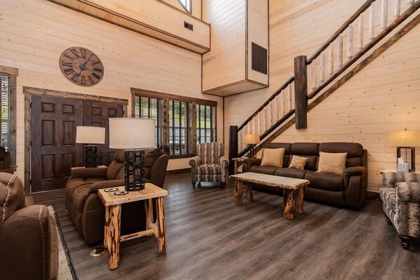 A spacious living room with a wooden floor, a large clock, and a staircase. - Private Indoor Pool & Basketball Court Retreat with Arcade Games, Sleeps 50, Free Tickets & Views (Branson)