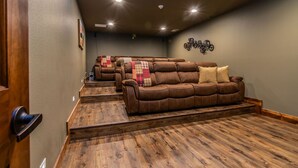 A home theater room with a brown leather couch, wooden flooring, and ceiling lights. - Private Indoor Pool & Basketball Court Retreat with Arcade Games, Sleeps 50, Free Tickets & Views (Branson)