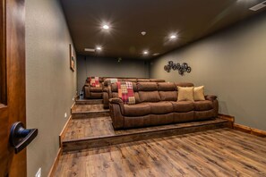 A home theater room with a brown leather couch, wooden flooring, and ceiling lights. - Private Indoor Pool & Basketball Court Retreat with Arcade Games, Sleeps 50, Free Tickets & Views (Branson)