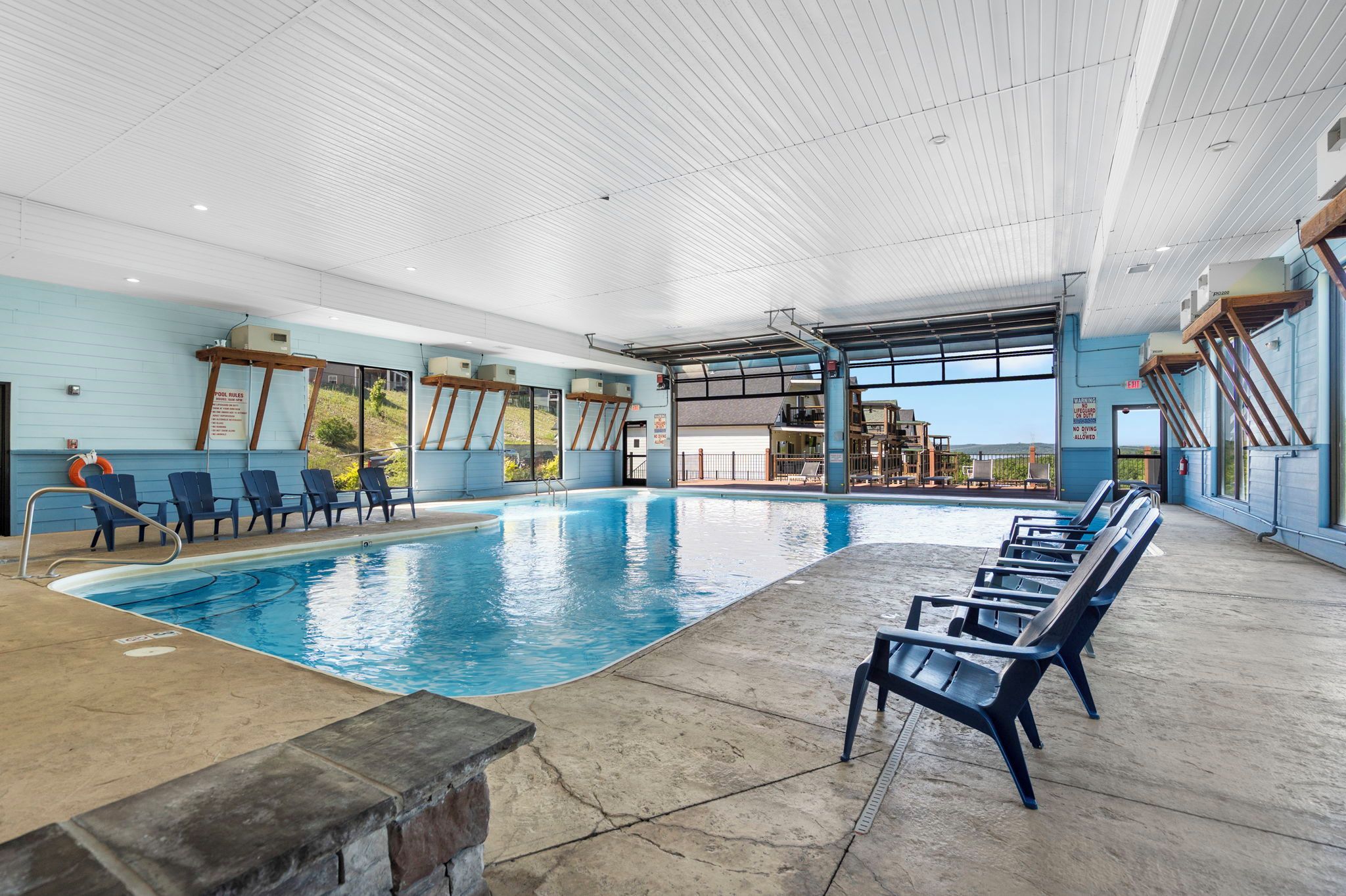 Una piscina interior con agua cristalina, rodeada de sillas de descanso y una zona cubierta con vistas al exterior.