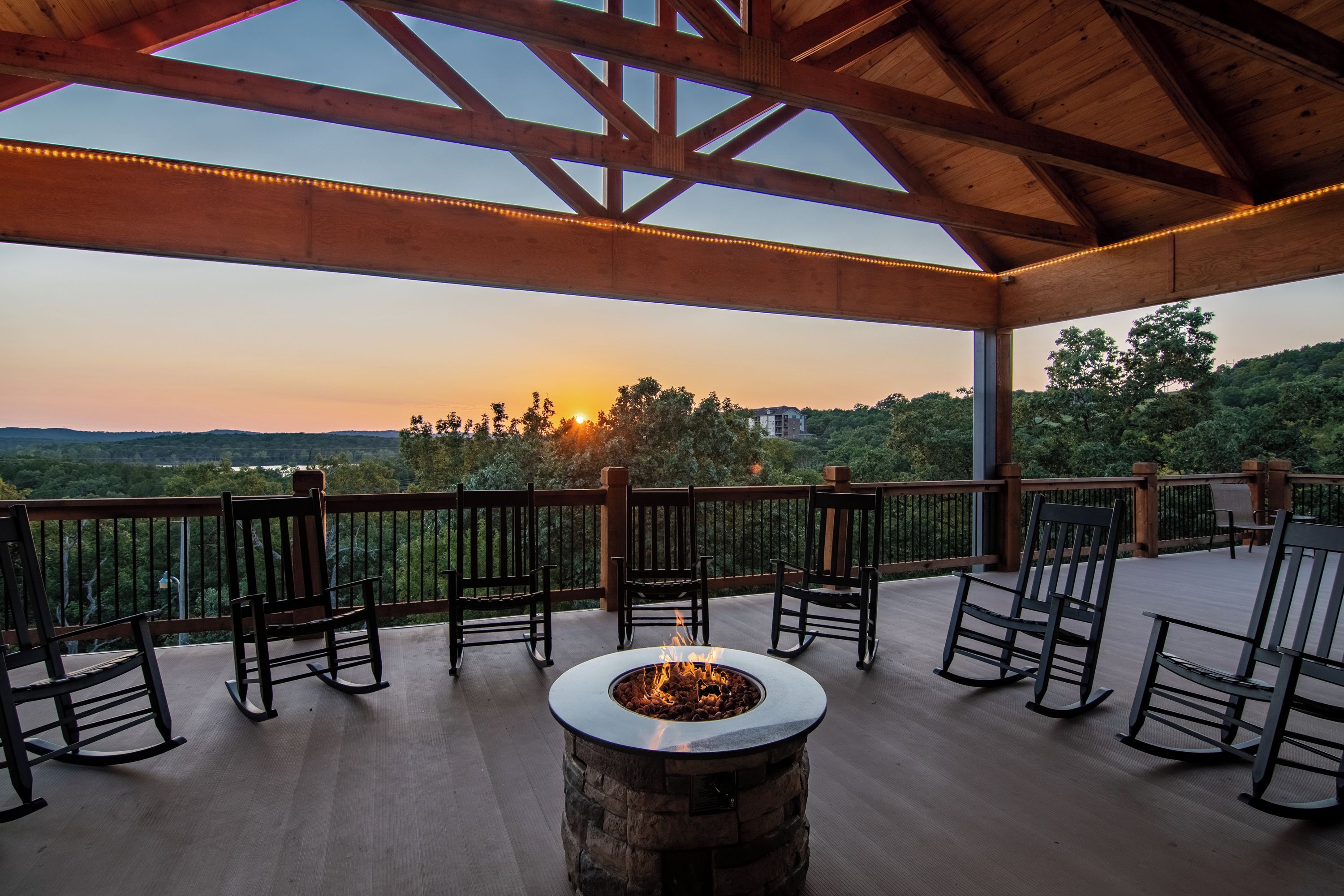 An outdoor deck with a fire pit and chairs, overlooking a scenic landscape.