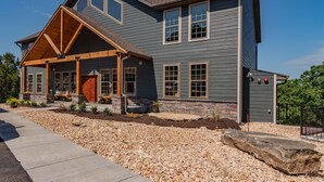 A two-story house with a stone foundation, a covered porch, and a large front yard with gravel and rocks. - Private Indoor Pool & Basketball Court Retreat with Arcade Games, Sleeps 50, Free Tickets & Views (Branson)