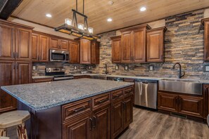 Una cocina con armarios de madera, encimera de granito, salpicadero de piedra, electrodomésticos de acero inoxidable y techo de madera.
