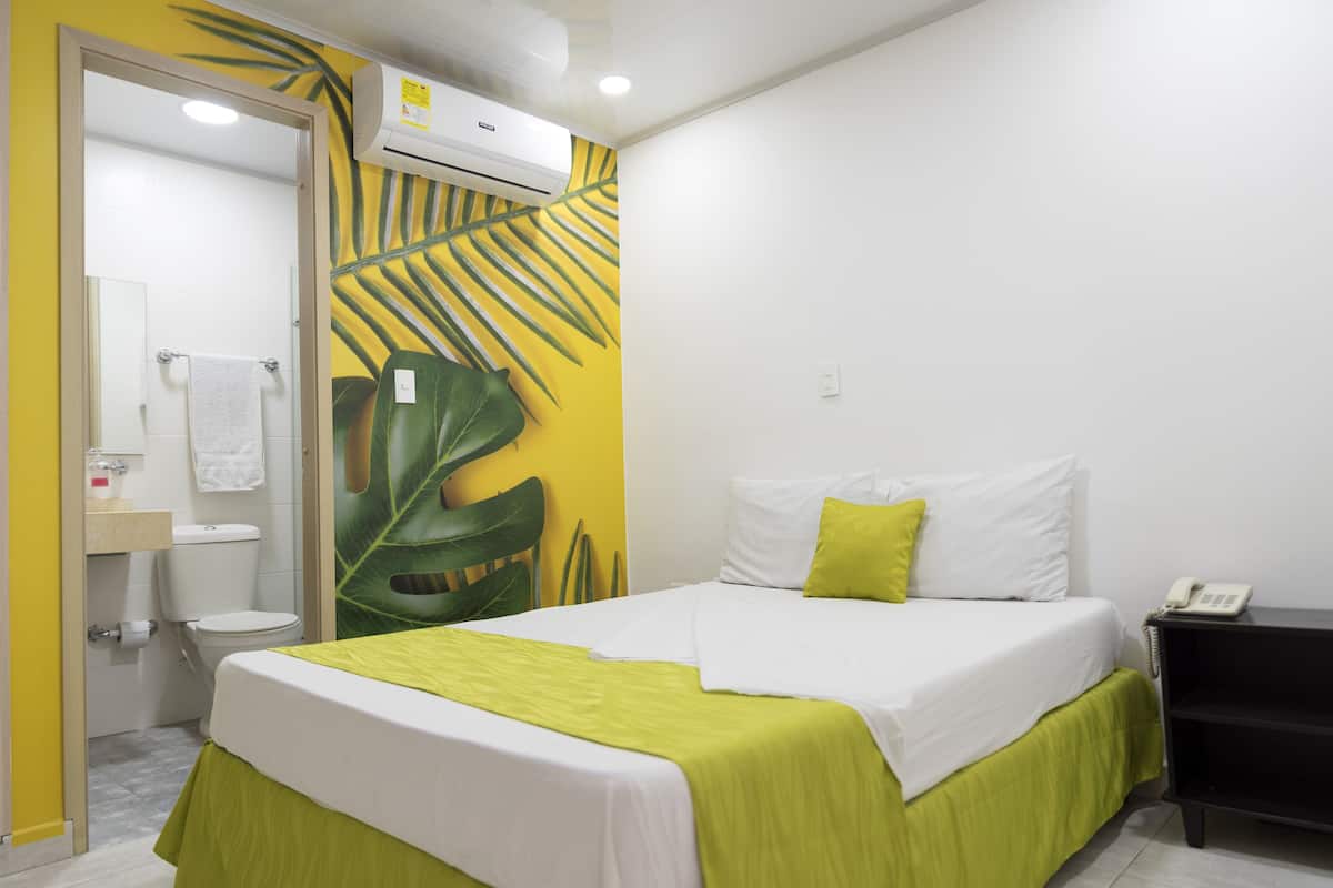 Habitación de hotel con cama, mesita de noche, teléfono y baño con inodoro y lavamanos.