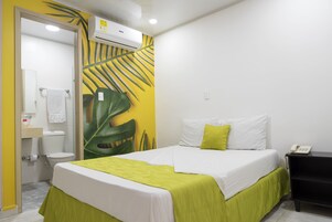 A hotel room with a bed, a bedside table, a phone, and a bathroom with a toilet and sink.