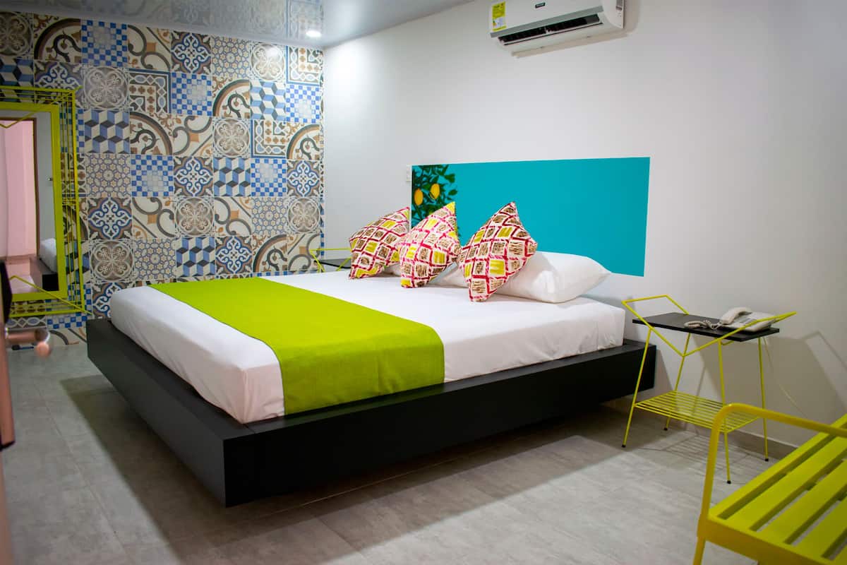 Un dormitorio moderno con cama, manta verde, almohadas estampadas, pared azul y una silla amarilla.
