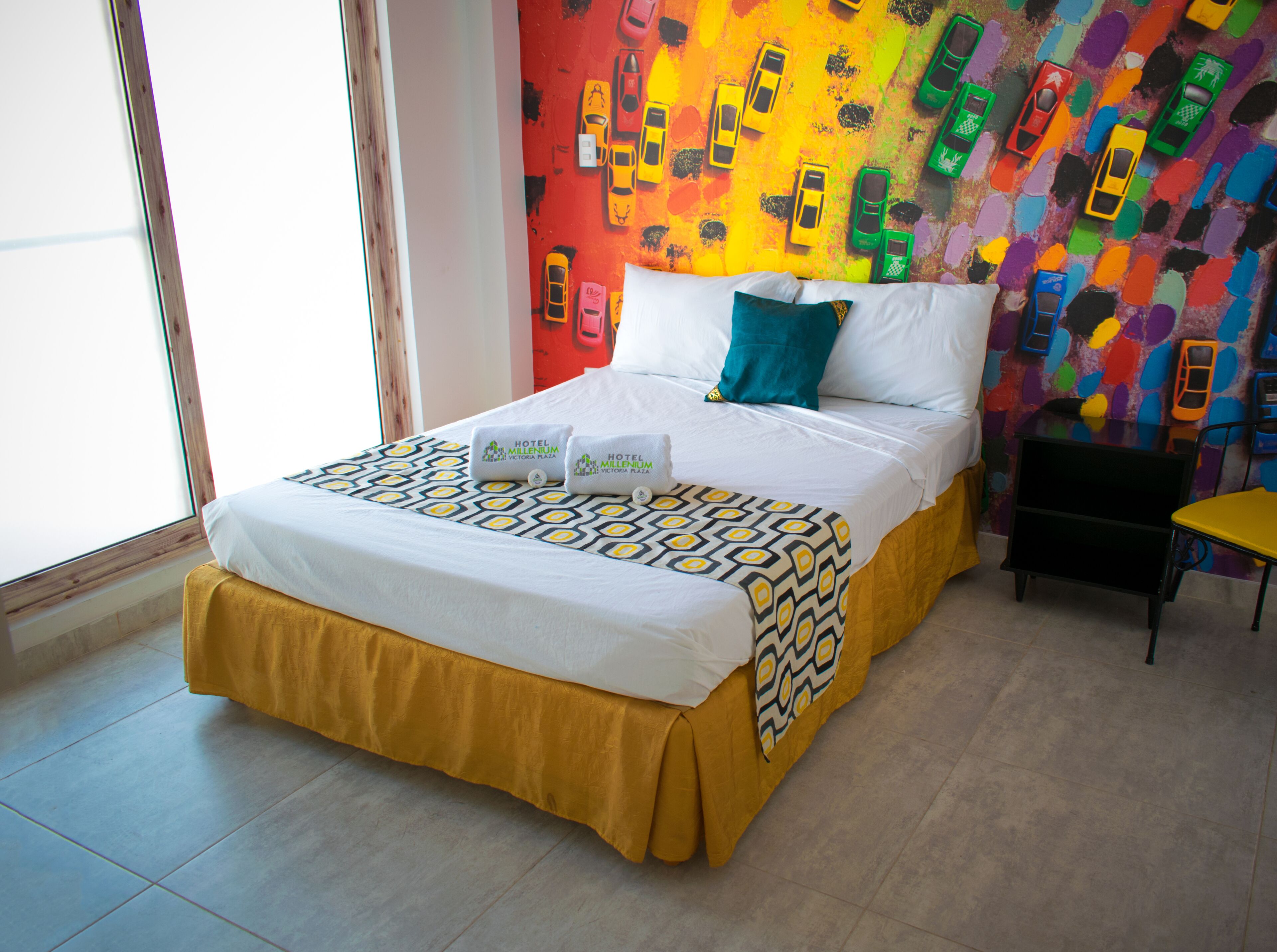 Una habitación de hotel con una cama, almohadas, una pared colorida y una mesita.
