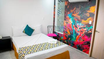 A hotel room with a bed, a nightstand, a colorful abstract mural, and a door.