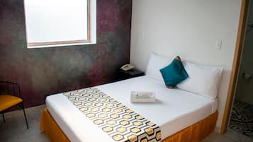 Una camera d'albergo con un letto, un comodino, un telefono, una finestra e una sedia.
