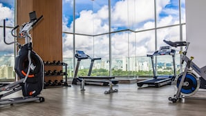 Et fitnessrum med løbeapparater, en vægmonteret vægtstang og udsigt over byen gennem store vinduer.