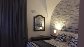Ein Schlafzimmer mit einer Steinsturz, einem Bett mit gemusterten Betttextilien, einem Nachttisch mit Lampe und einem Spiegel an der Wand.