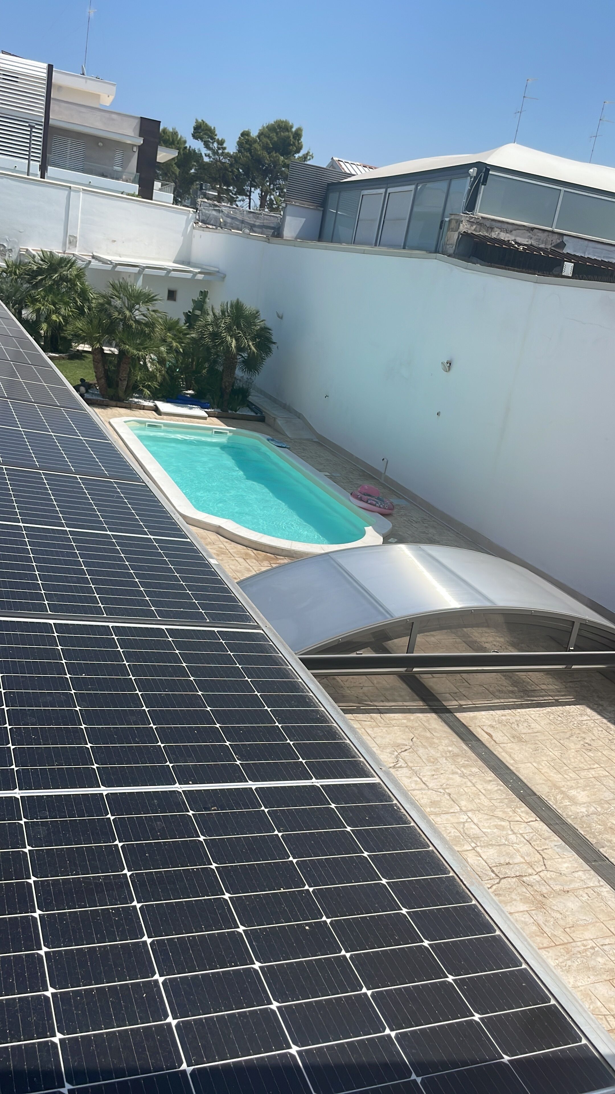 Eine Dachterrasse mit Solaranlage, einem Swimmingpool und einer weißen Wand.