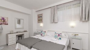 Un dormitorio con cama, mesitas de noche, cómoda, espejo e iluminación en la pared.