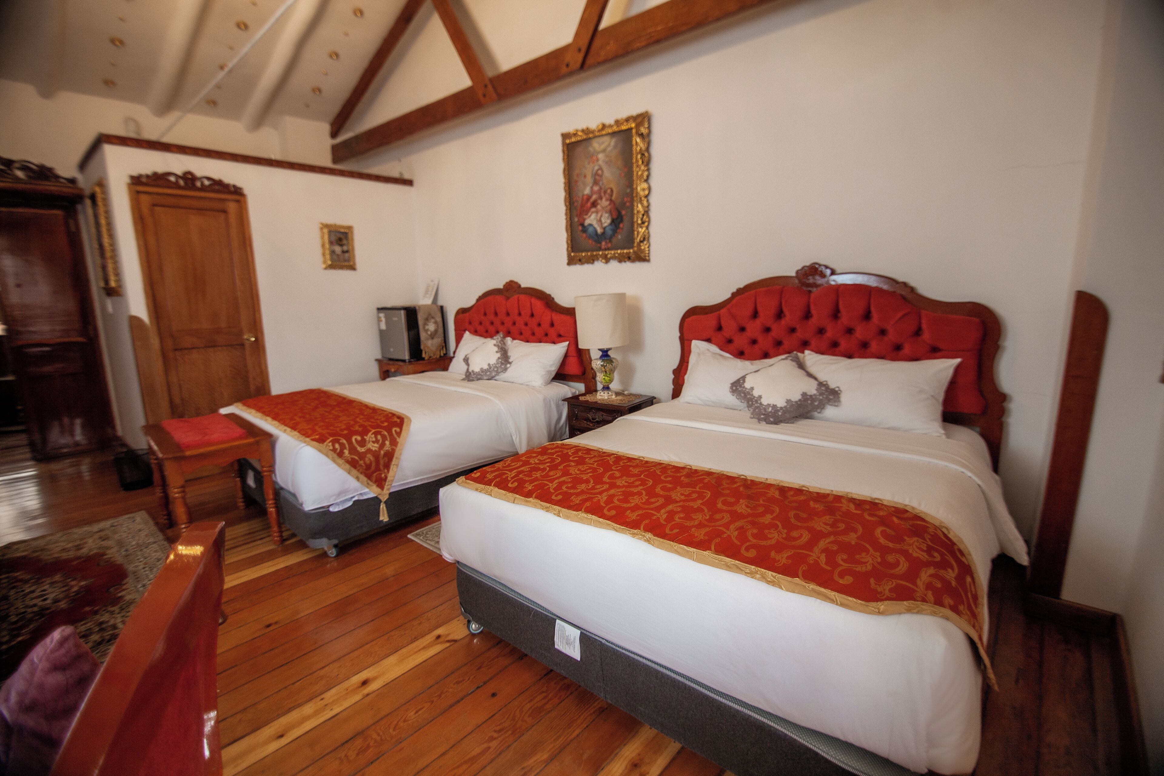 A hotel room with two beds, wooden flooring, a wooden wardrobe, a desk, and a chair.