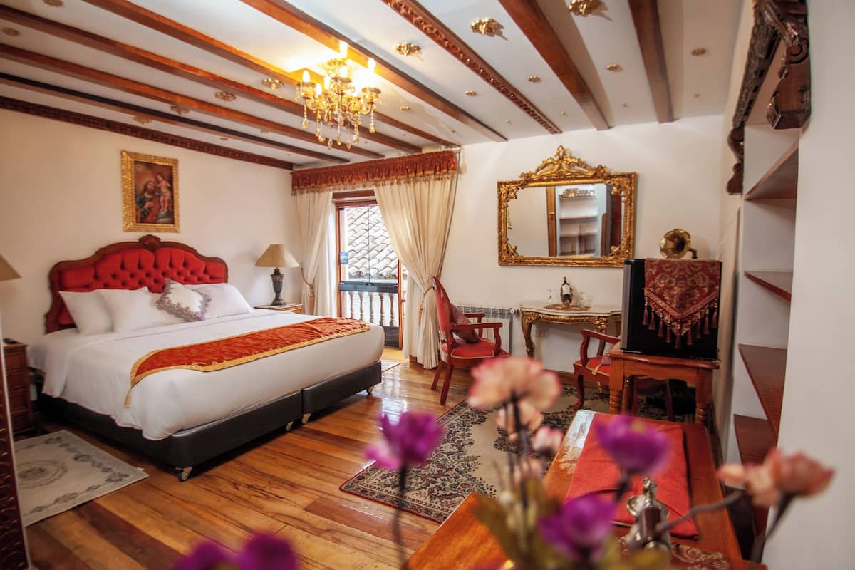 Un dormitorio con una cama grande, techo de madera, candelabro, espejo y un escritorio con silla.