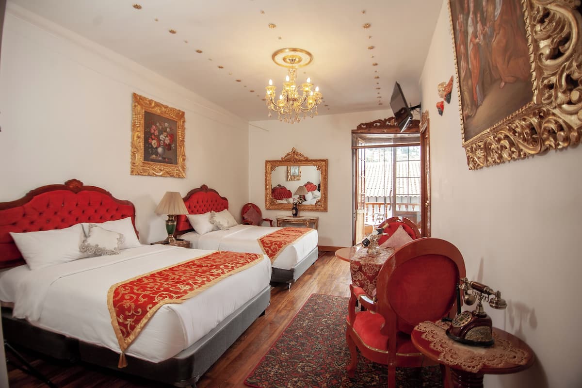 Una habitación de hotel con dos camas, un candelabro, un escritorio con teléfono y un espejo grande.