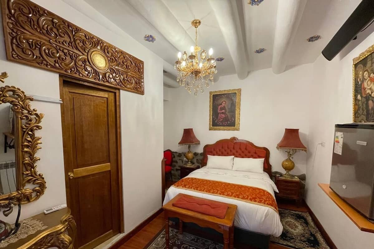 Un dormitorio con una cama grande, una puerta de madera, una araña, un televisor y un espejo con marcos ornamentados.