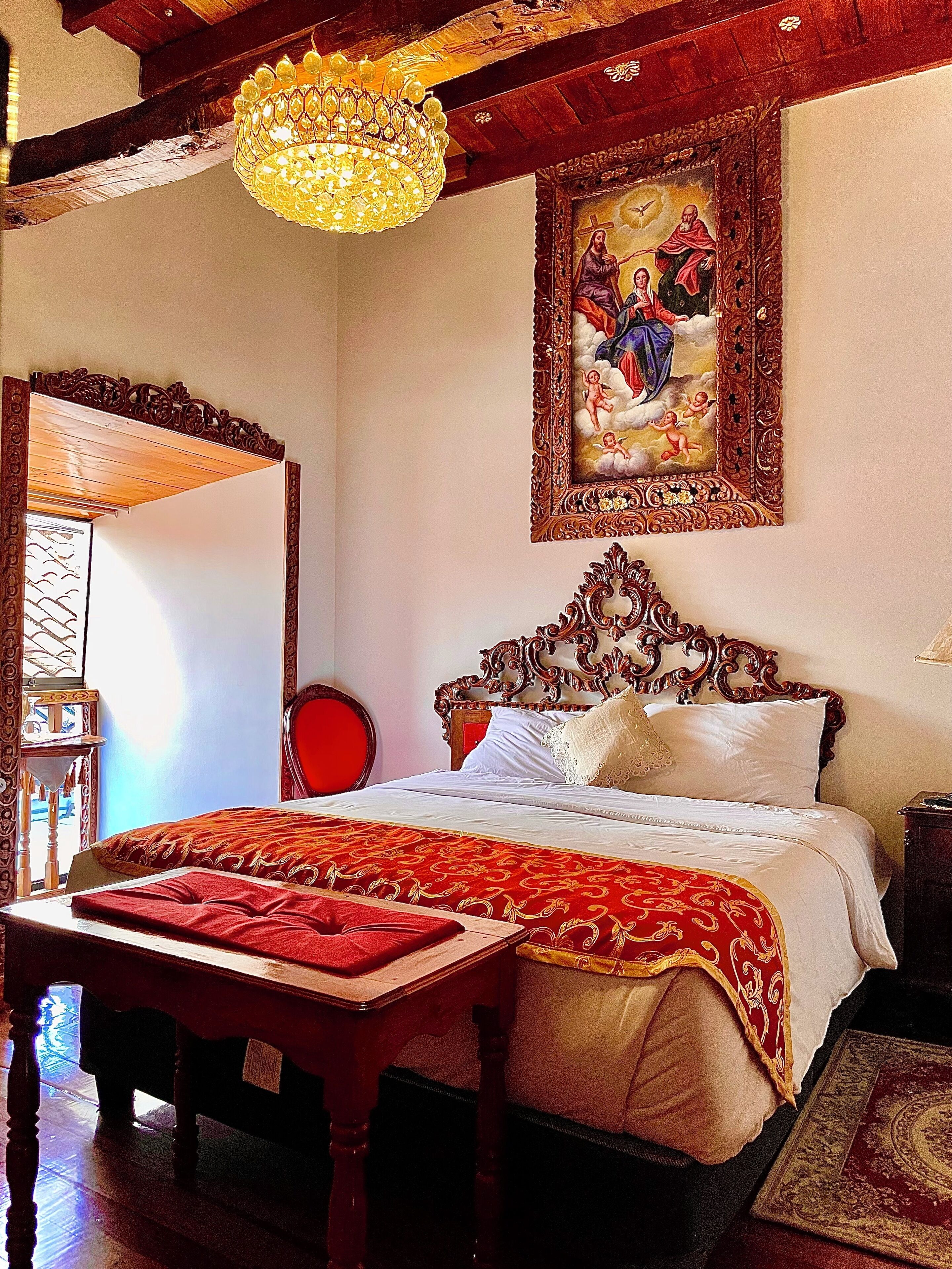 Una habitación tradicional con una cama de madera, una araña y un cuadro religioso en la pared.