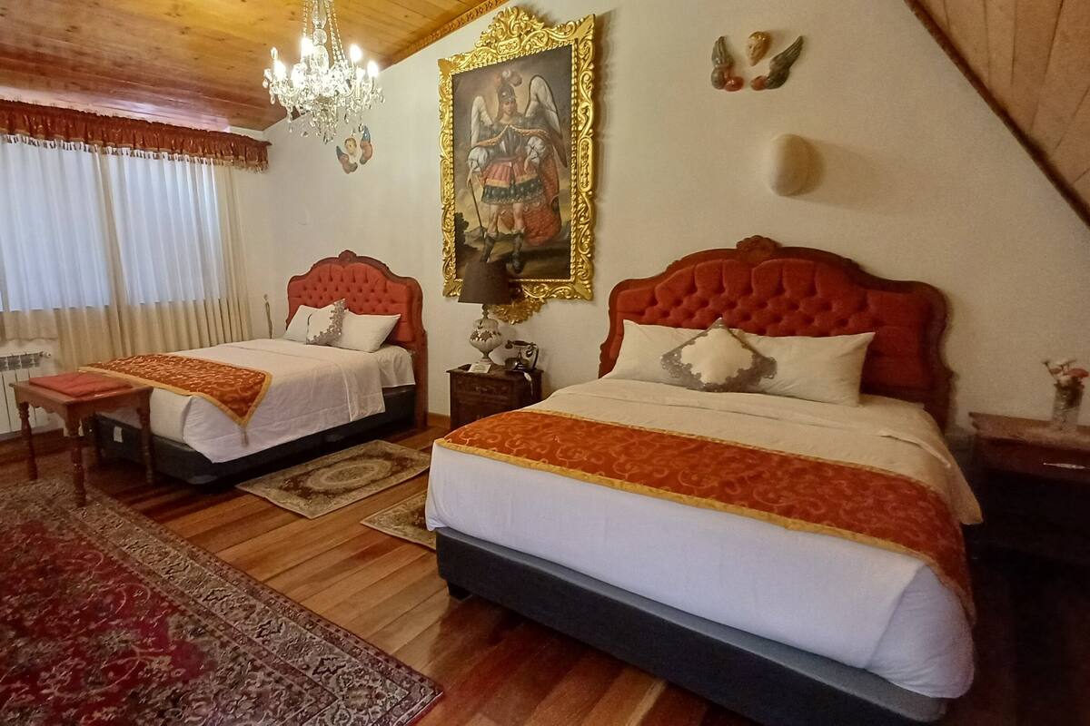 Habitación de hotel con dos camas, un candelabro, un radiador y un cuadro grande en la pared.