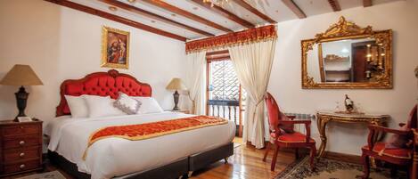 A bedroom with a large bed, wooden beams, a chandelier, a red upholstered headboard, a mirror, and a small table.