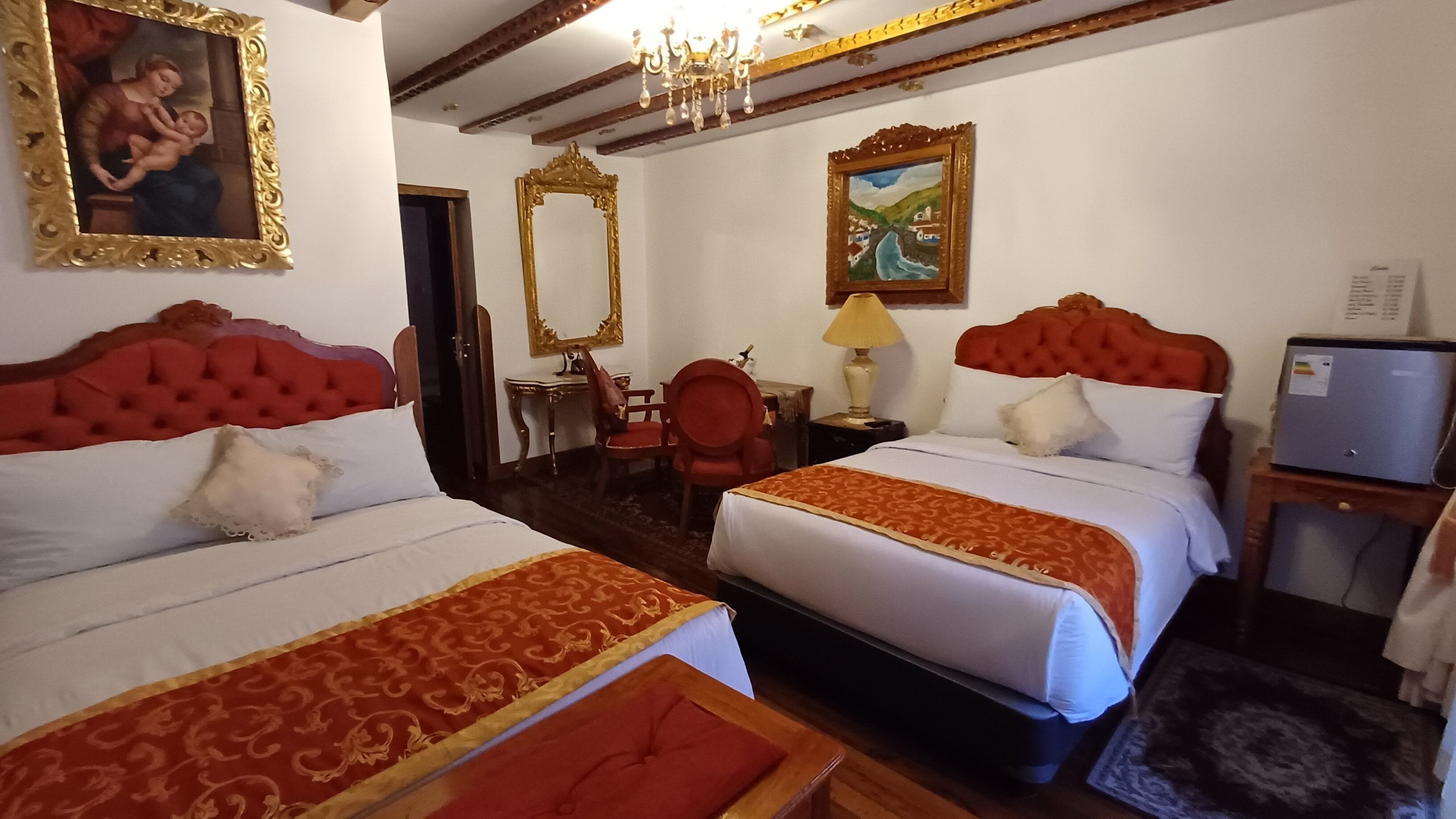 A hotel room with two beds, a desk, a chair, a mirror, and a painting on the wall.