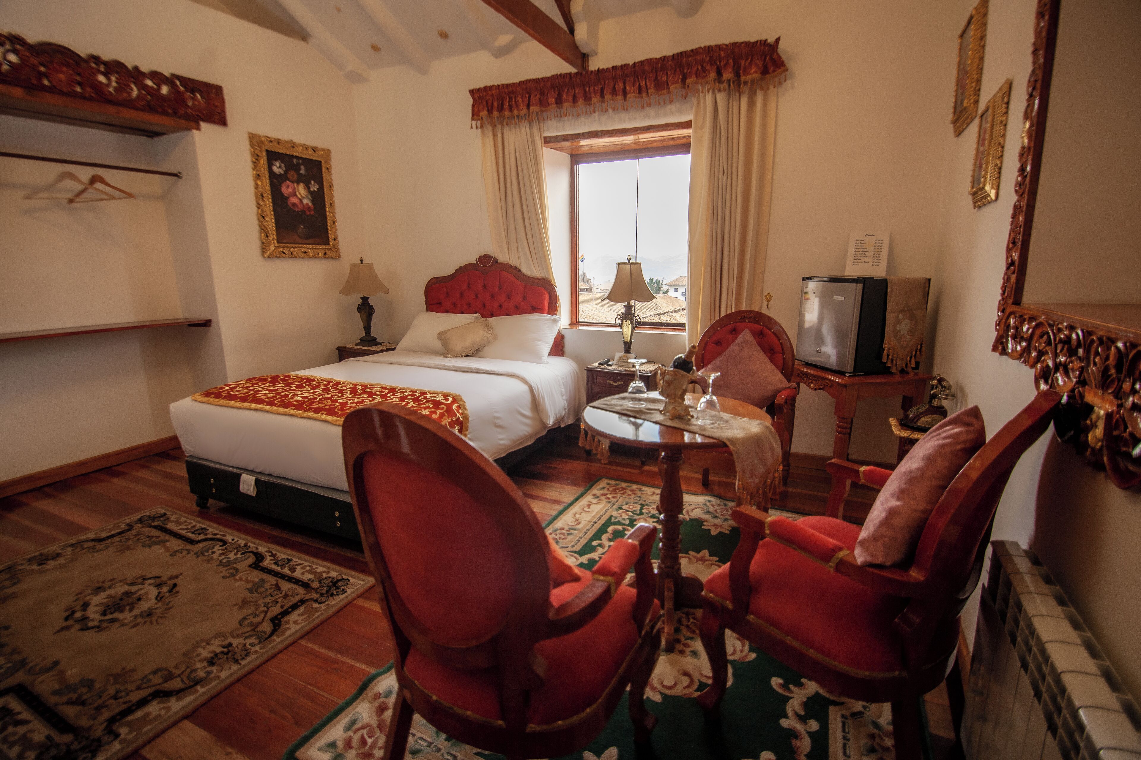 Habitación de hotel con una cama, dos sillas, una mesa, una lámpara, un televisor y un ventanal con cortinas.