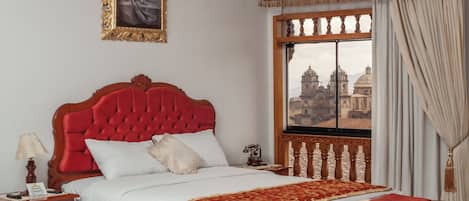 A hotel room with a large bed, a wooden nightstand, a table, and a window with a view of a cityscape.