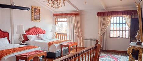 Una habitación de hotel con dos camas, una araña, un ventanal grande con cortinas y un suelo de madera tradicional.