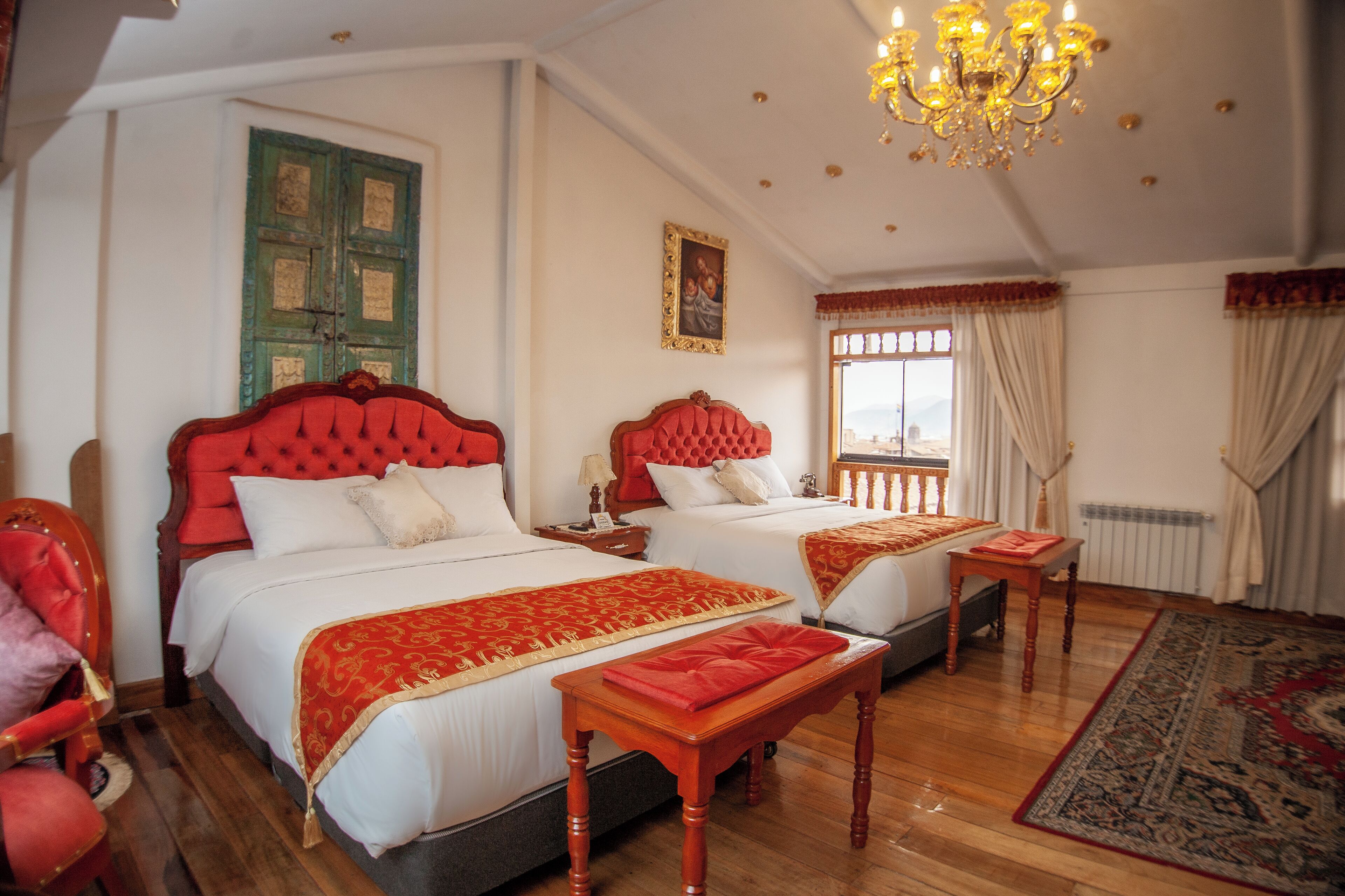 Une chambre d’hôtel avec deux lits, un lustre, un plancher en bois et une grande fenêtre avec des rideaux.