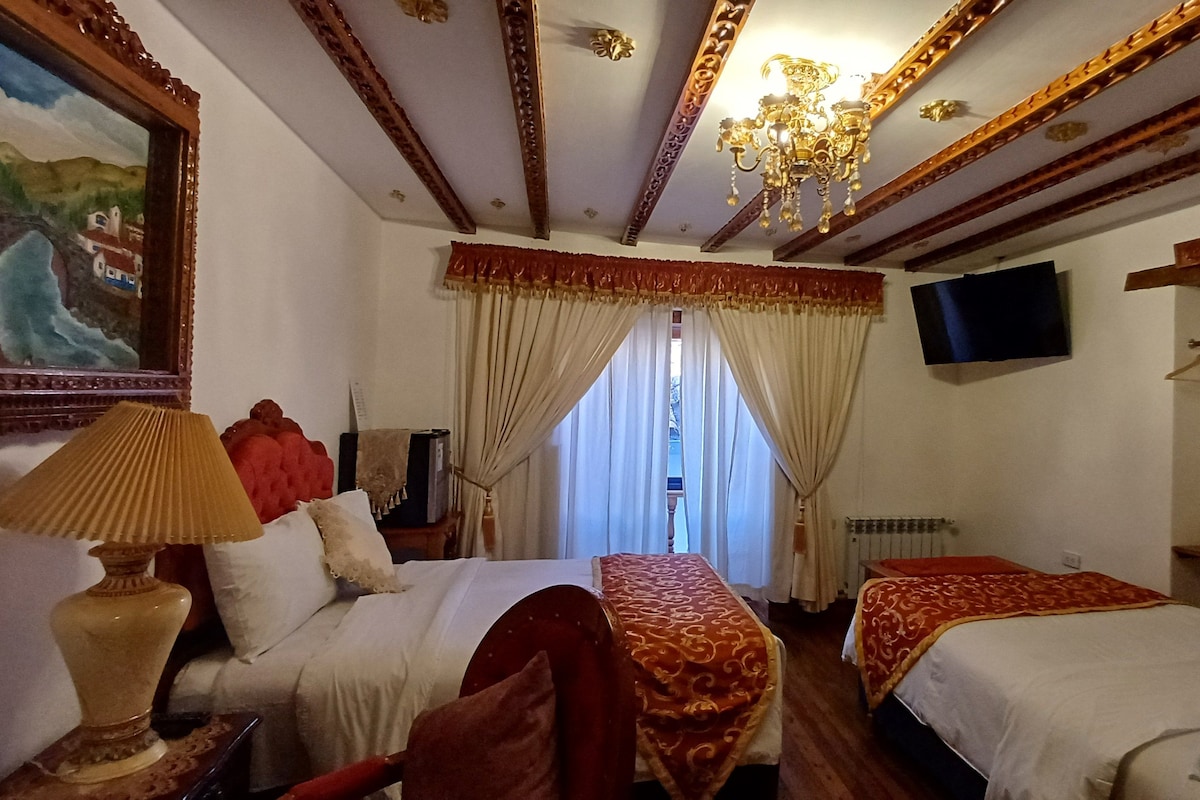 A hotel room with two beds, a painting, a chandelier, and a television on the wall.