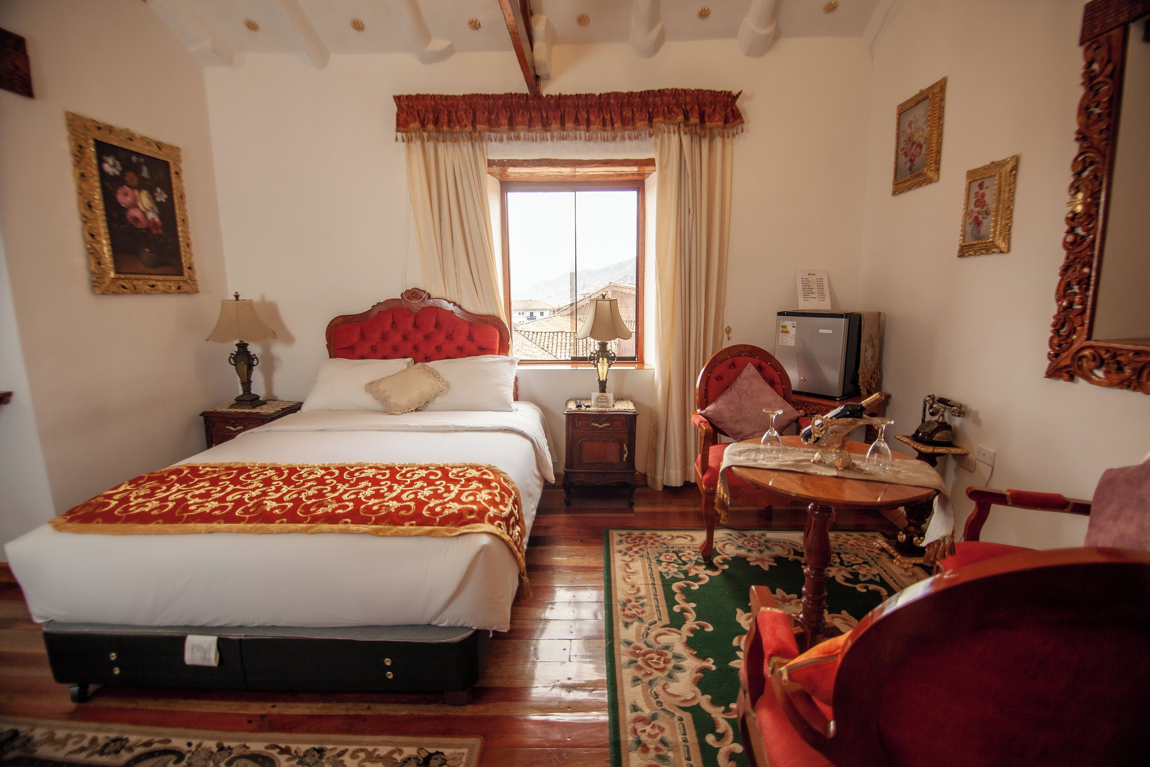 Habitación de hotel con cama, escritorio con lámpara, silla, televisor y ventana con cortinas.