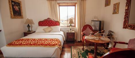 Habitación de hotel con cama, escritorio con lámpara, silla, televisor y ventana con cortinas.