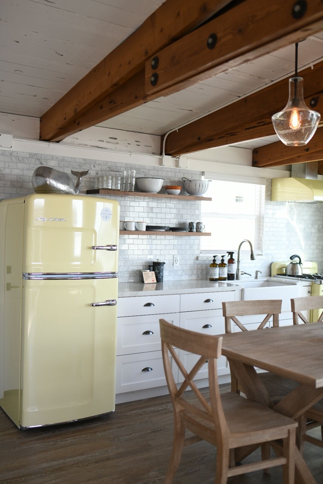 A kitchen with a yellow refrigerator, wooden chairs, a wooden table, and a hanging light fixture.