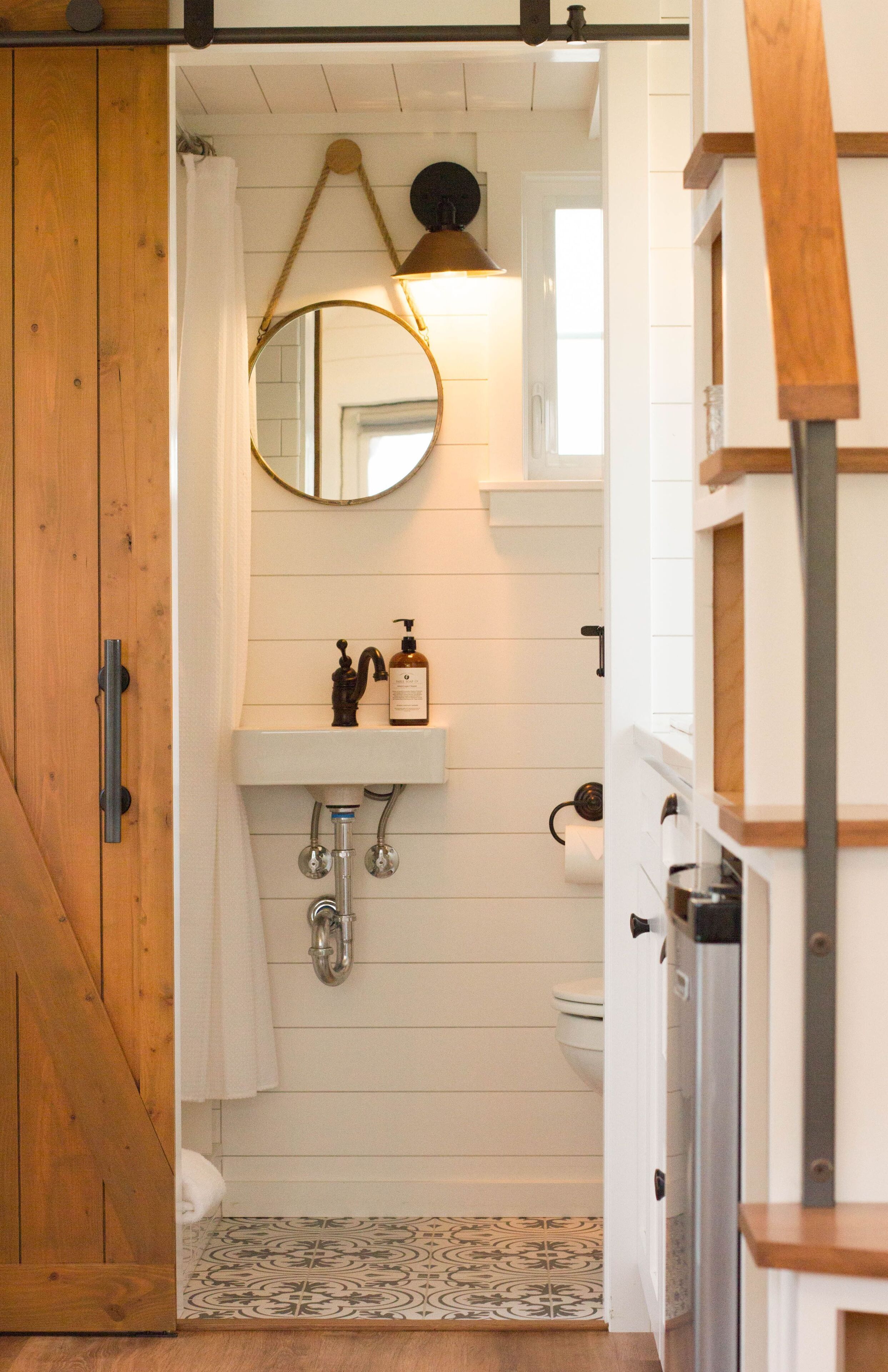 Un baño con puerta de madera, un lavamanos blanco con espejo y un inodoro.