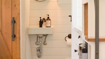 Un baño con puerta de madera, un lavamanos blanco con espejo y un inodoro.