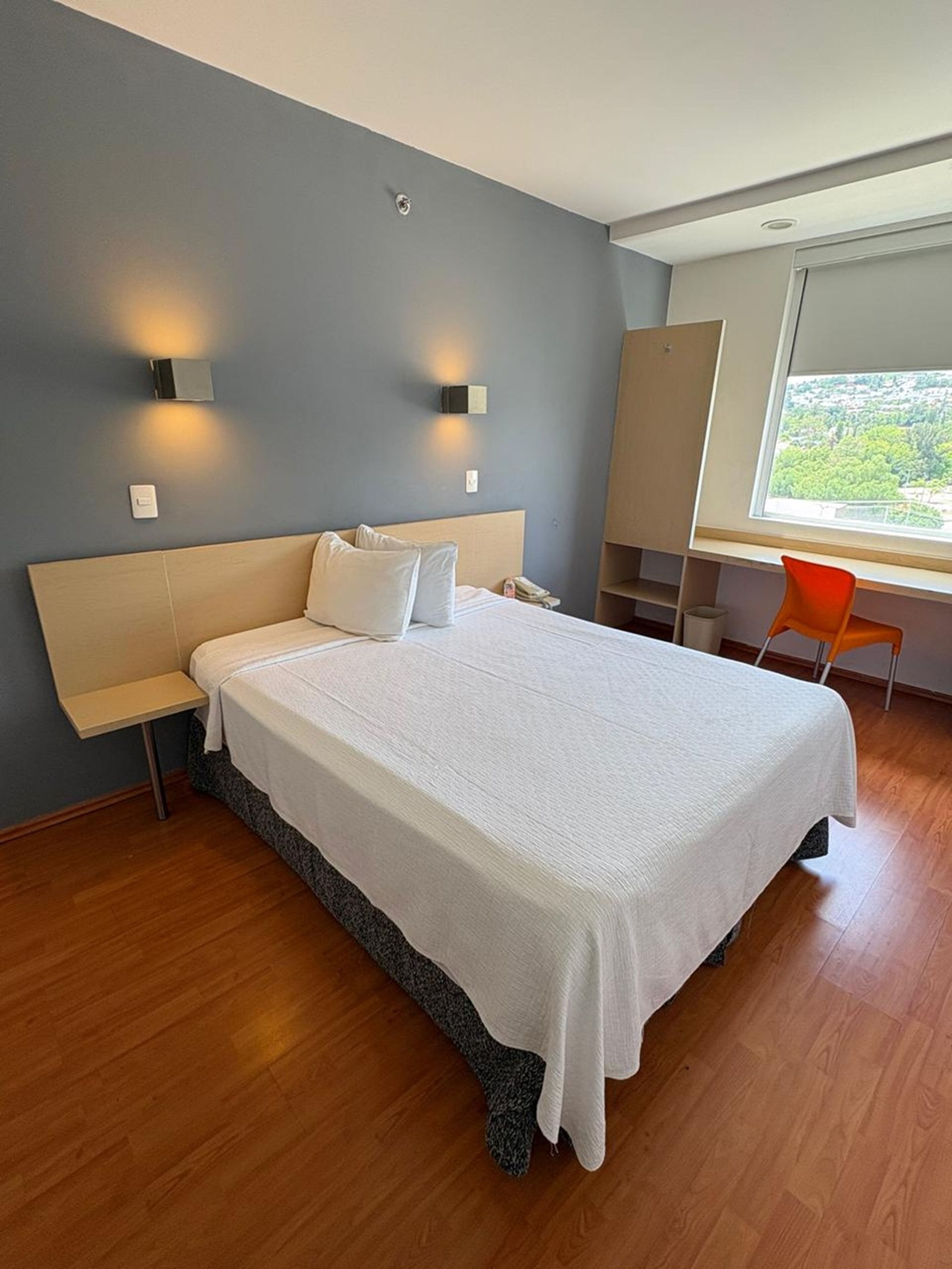 A modern hotel room with a large bed, bedside tables, a desk, and a chair.
