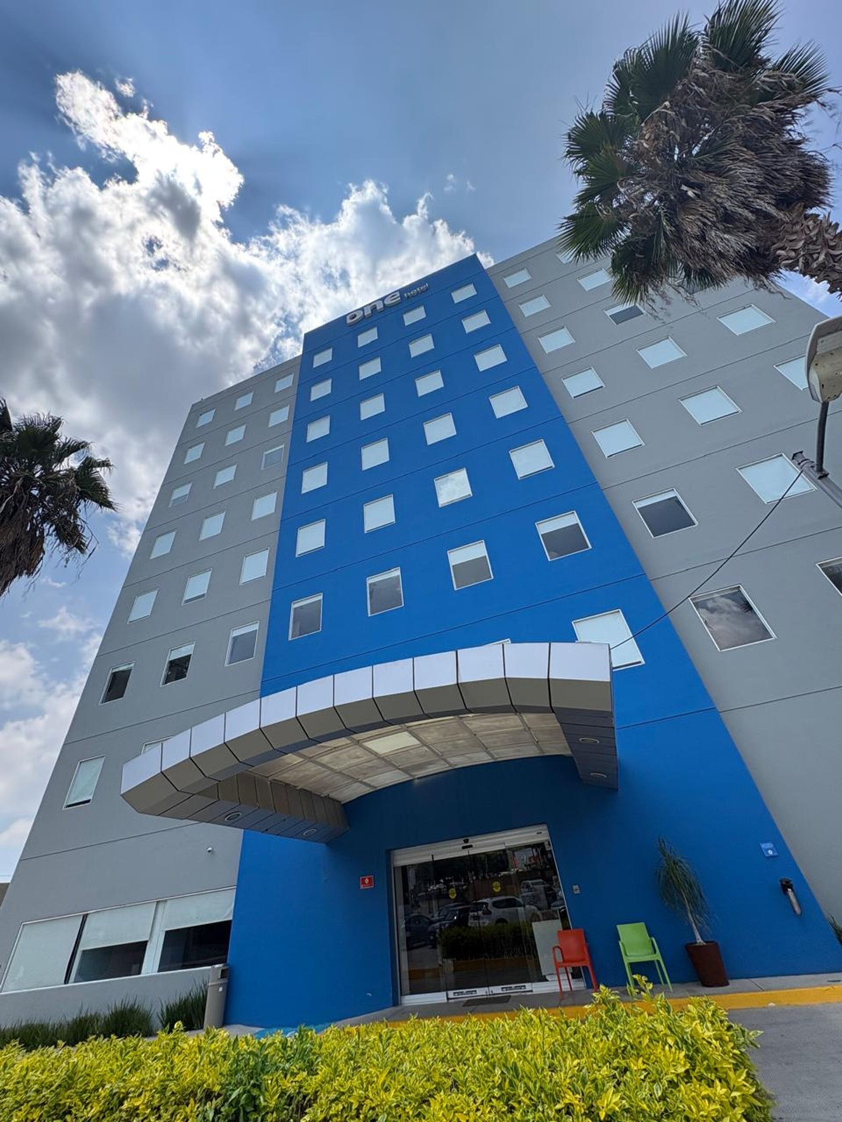 A modern hotel with a blue and grey facade, multiple windows, and a covered entrance.
