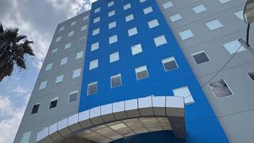 A modern hotel with a blue and grey facade, multiple windows, and a covered entrance.