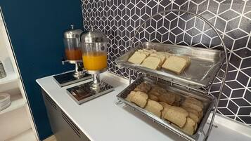 A breakfast buffet with juice dispensers, sandwiches, and pastries.