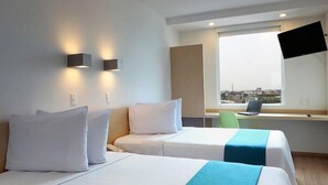 A hotel room with two beds, a desk, a chair, and a TV mounted on the wall. - One Irapuato (Irapuato)
