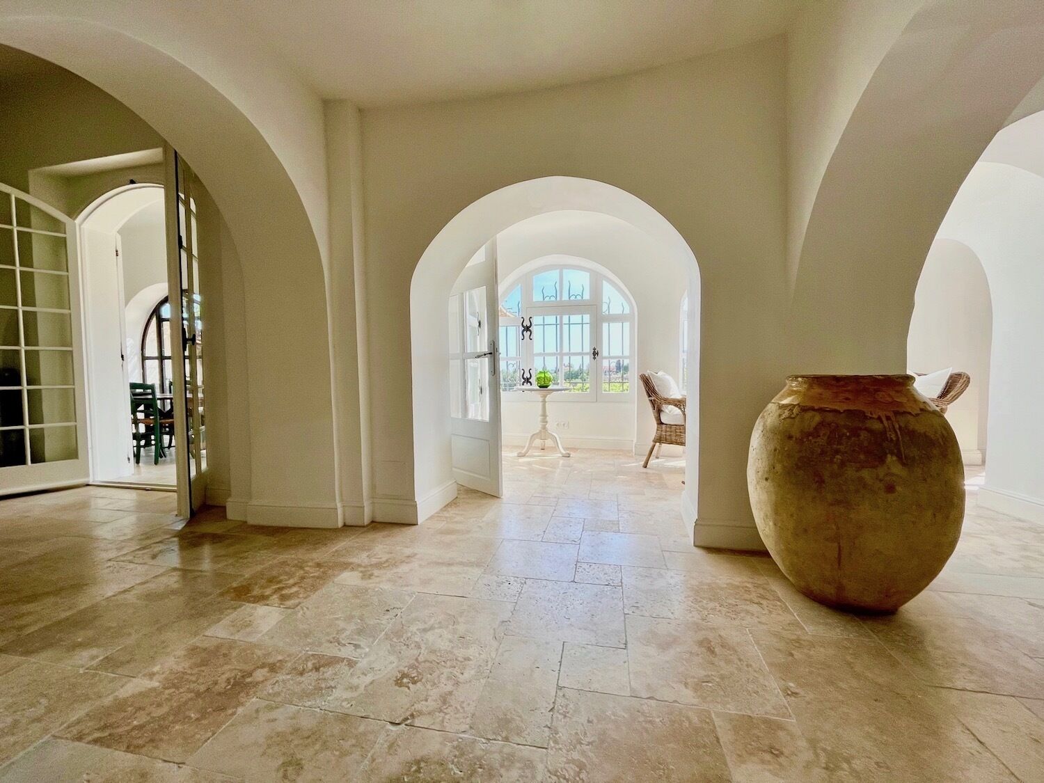 Un intérieur spacieux avec des portes en arc de cercle, un grand vase et une vue par la fenêtre.
