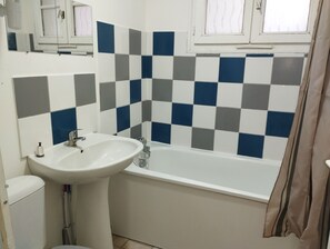 A bathroom with a white sink, a bathtub, and a tiled wall with a checkered pattern. - La Belle Onde (Dieppe)