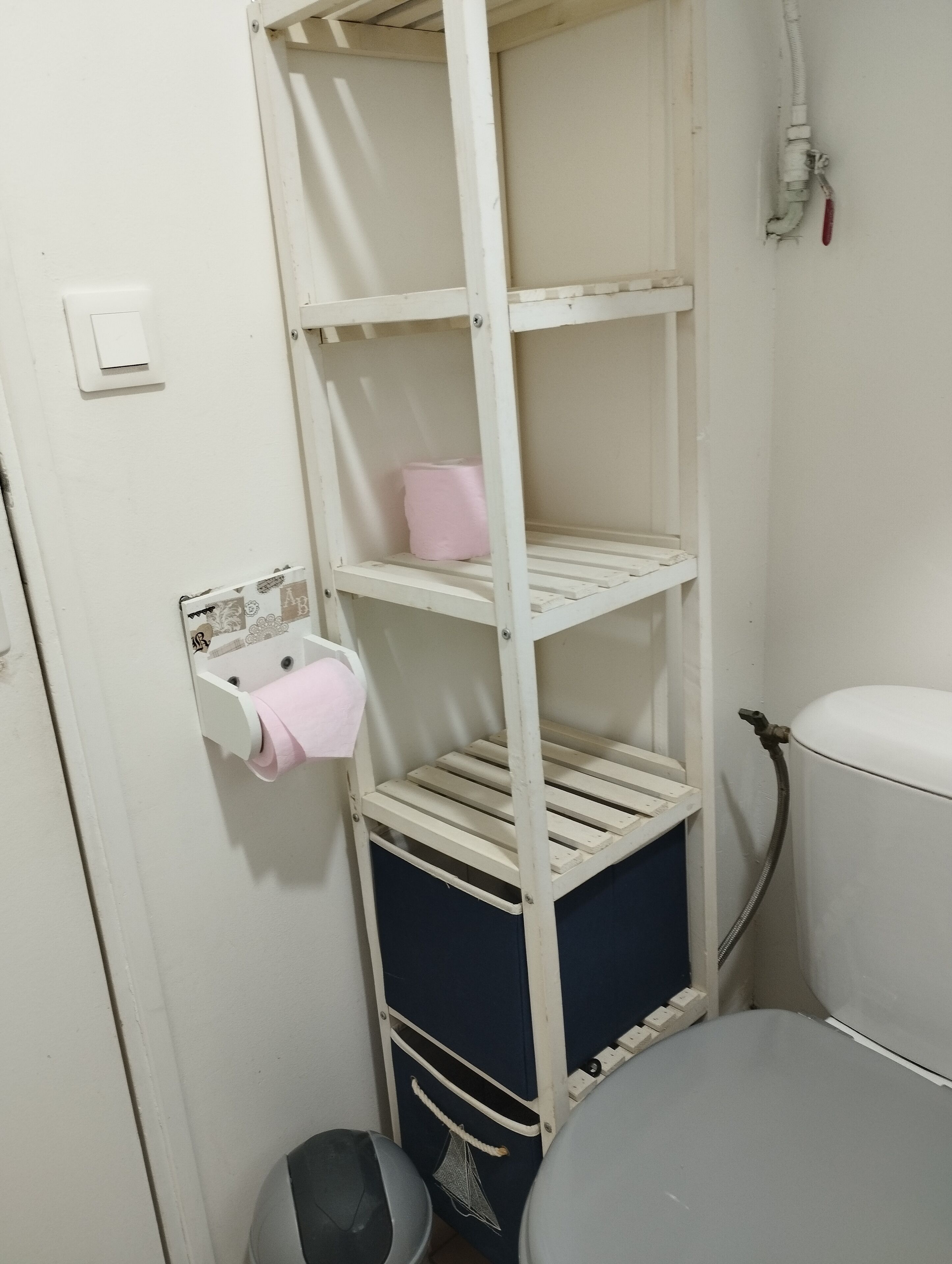 A white metal shelf unit with a pink tissue holder and a blue storage box.